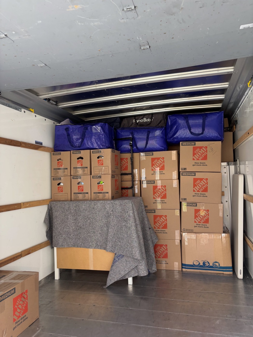 Interior de un camión cargado con muebles cubiertos por cobijas y cajas ordenadas por tamaño