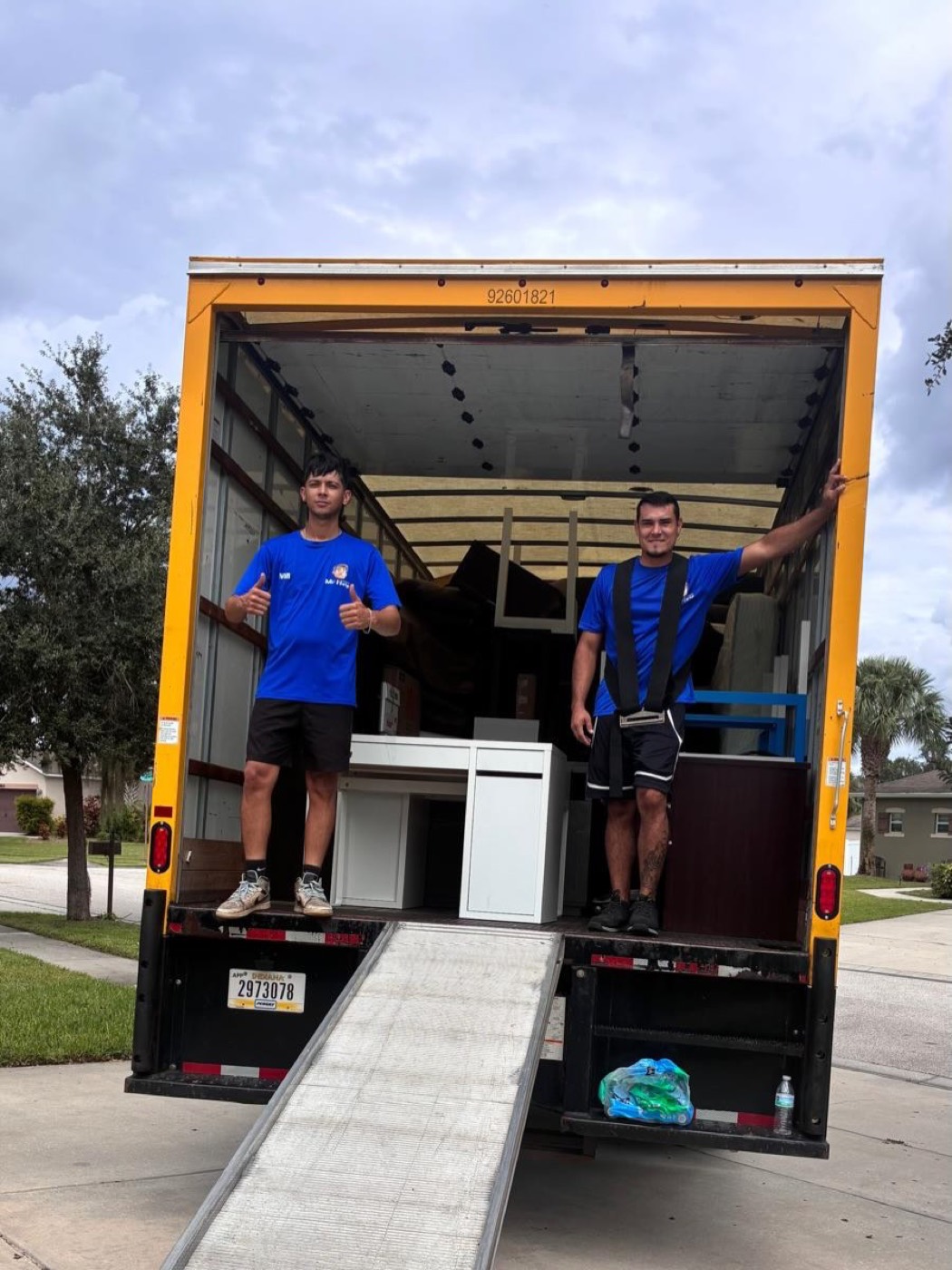 Dos miembros del equipo de Solutions Mr.Help con camisas azules sobre la rampa de un camión de mudanza cargado