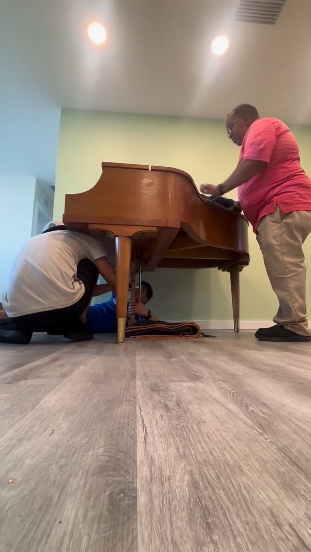 Equipo envolviendo y levantando un piano de cola dentro de una casa