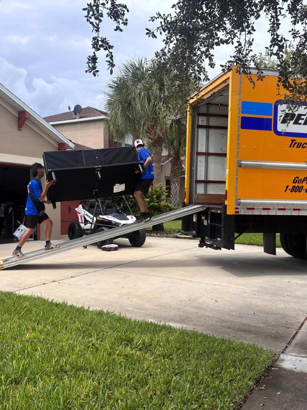 Dos trabajadores bajando un mueble grande envuelto por la rampa del camión frente a una casa en Florida